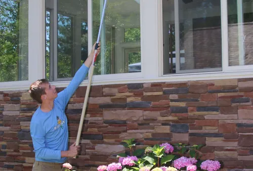 Pest control technician removing spider webs from a porch at a Great Falls estate near Georgetown Pike
