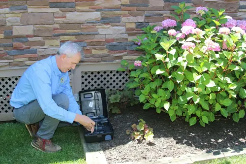 Technician servicing a rodent bait station at a Great Falls property near Difficult Run with flowers in foreground